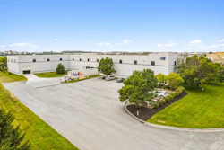 Large industrial warehouse facility with FedEx delivery truck in parking lot surrounded by manicured landscaping
