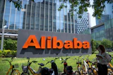 Alibaba orange logo sign displayed in urban plaza with yellow bicycles and modern skyscrapers
