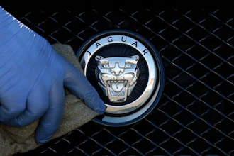 A worker polishes a Jaguar logo on a car at a Jaguar dealer in London, Wednesday Sept. 28, 2016.