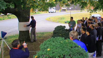 Public demonstration of a large invisibility cloak, showing the cloaking structure being positioned around a tree before an audience. This demonstration, where this portion of the tree disappeared at microwaves, was arranged and witnessed by radar boffin Dr. Eli Brookner and the IEEE Phased Array Conference participants.
