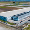 Aerial view of modern industrial warehouse and logistics facility complex with blue and white buildings in rural landscape