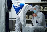Worker in white protective suit and mask in industrial facility with shelved products and ABM branded clothing visible