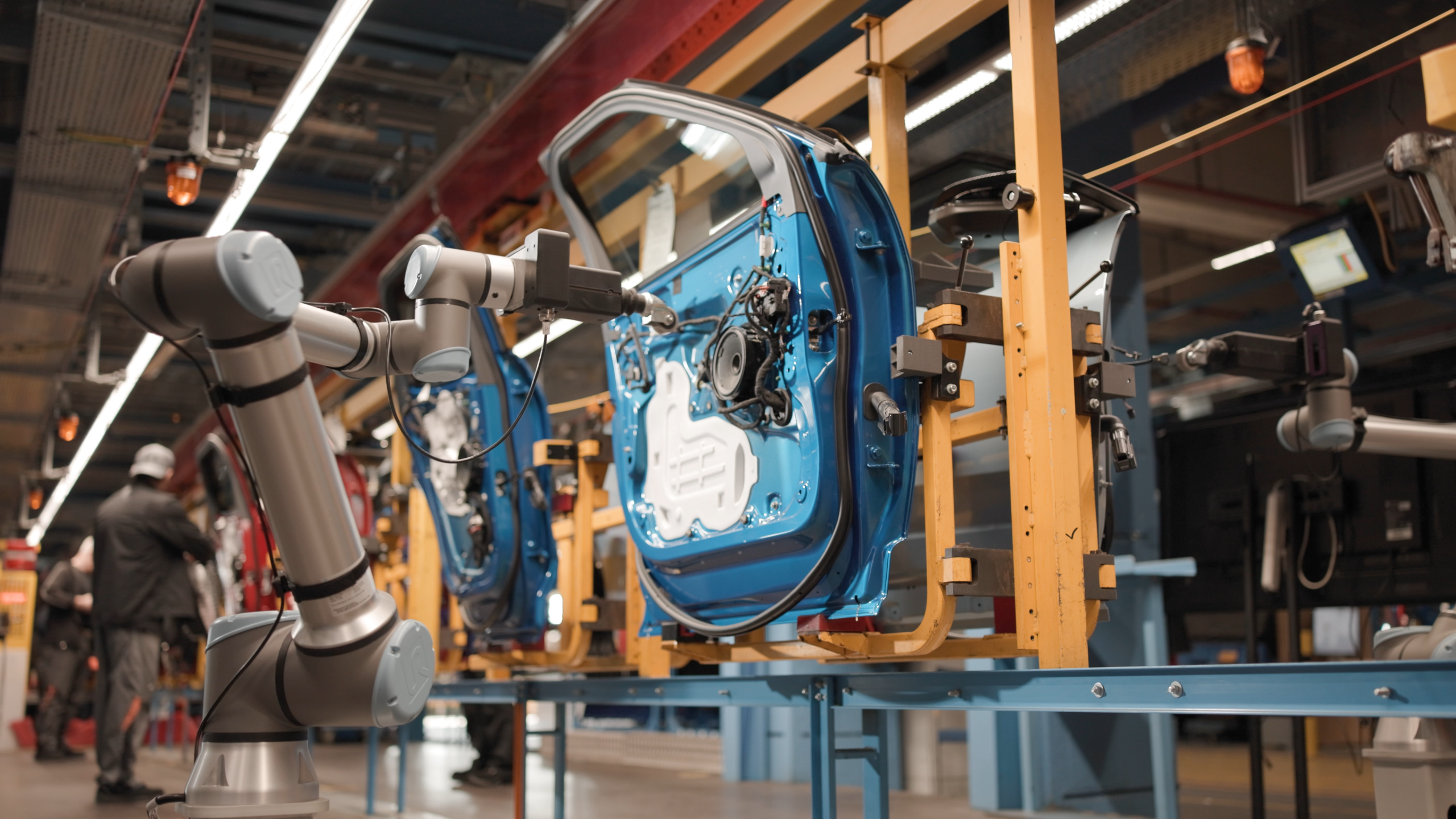 Robotic arms assembling blue car door on factory assembly line