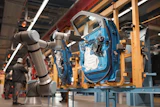 Robotic arms assembling blue car door on factory assembly line