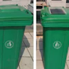 Two green recycling bins with white circular emblems on a paved outdoor surface