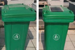 Two green recycling bins with white circular emblems on a paved outdoor surface