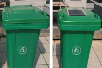 Two green recycling bins with white circular emblems on a paved outdoor surface
