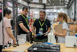 Trade show booth demonstration with staff and visitors examining tools and equipment at an industrial exhibition