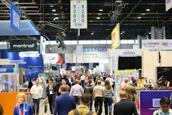Crowded trade show exhibition floor with multiple vendor booths, signage, and professional attendees networking in an indoor convention center.