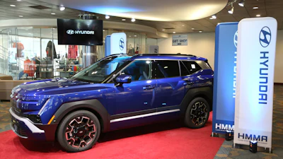 Blue Hyundai Kona electric vehicle displayed in modern showroom with branded signage and red carpet