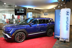 Blue Hyundai Kona electric vehicle displayed in modern showroom with branded signage and red carpet