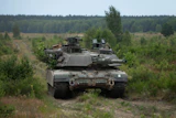 Military tank positioned in forested terrain with coniferous trees and cleared ground in background