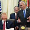 Formal meeting in the Oval Office with government officials and American flags in background