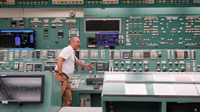 Technician operating control room with extensive monitoring equipment and instrument panels