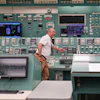 Technician operating control room with extensive monitoring equipment and instrument panels