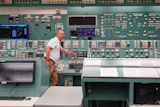 Technician operating control room with extensive monitoring equipment and instrument panels