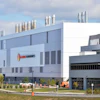 Modern industrial facility with Helios Technologies signage, featuring blue and white architecture with cylindrical ventilation stacks on the roofline.