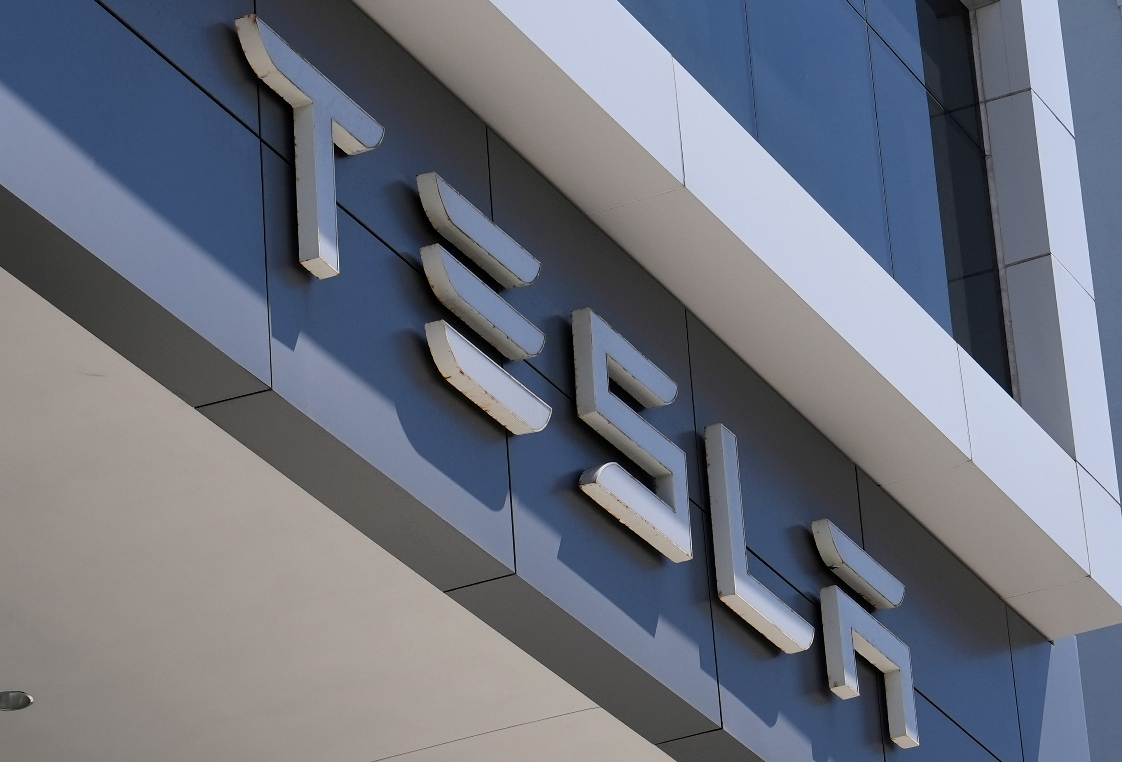 Three-dimensional white lettering mounted on modern blue and white building facade with shadow details