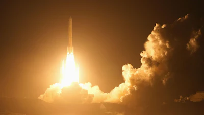Rocket launching at night with bright engine flames piercing through golden clouds over the ocean