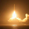 Rocket launching at night with bright engine flames piercing through golden clouds over the ocean