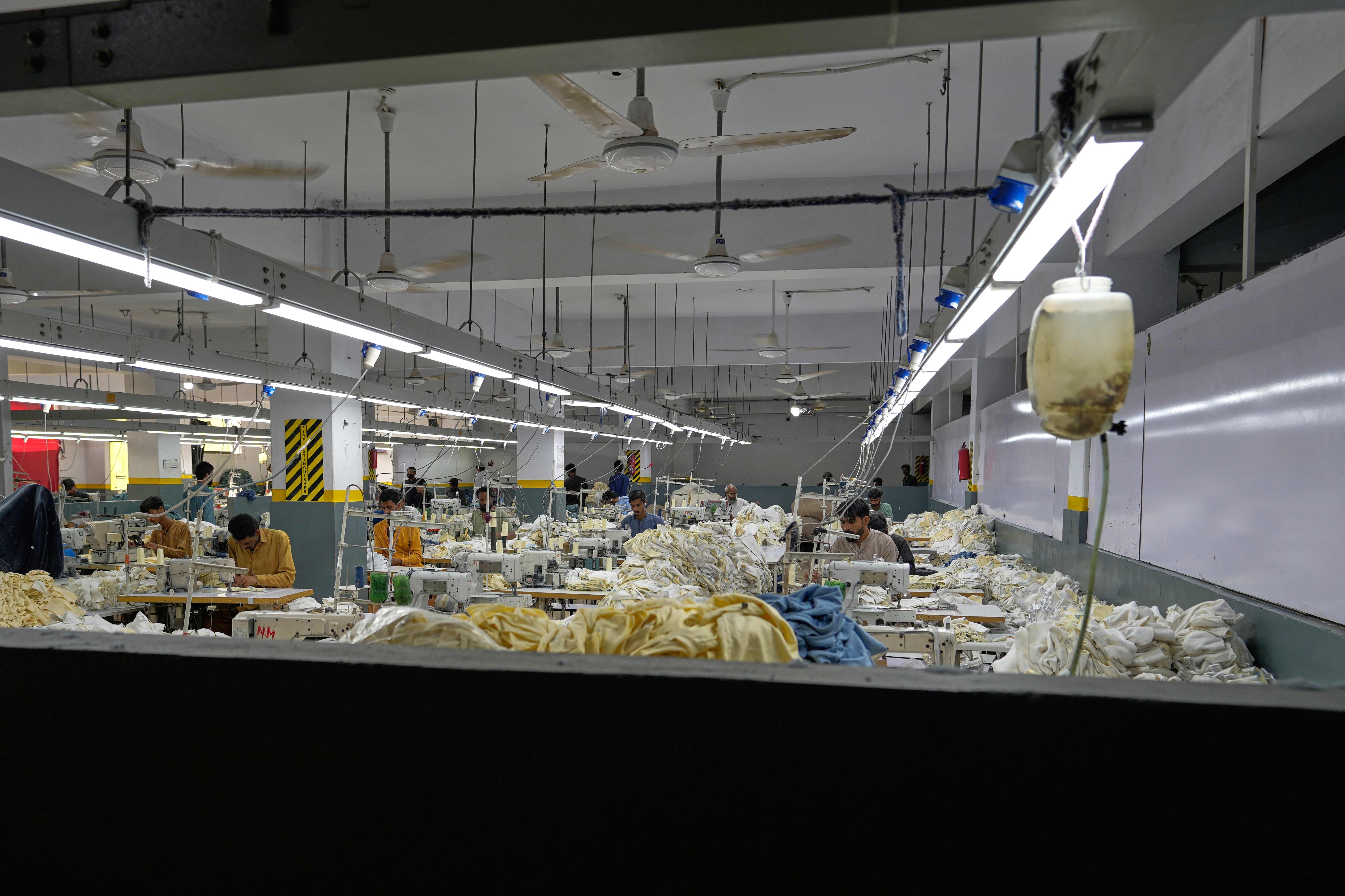 Industrial textile factory floor with workers processing fabrics at production stations under bright overhead lighting