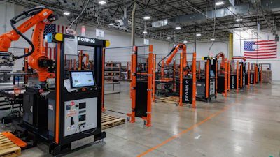 Industrial robotic welding facility with orange automation equipment and American flag in warehouse setting