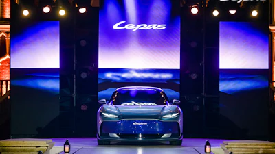 Luxury sports car displayed on stage during brand launch event with illuminated screens and dramatic blue lighting