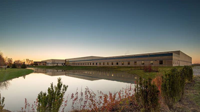 Modern industrial building complex reflected in calm water at dusk with autumn vegetation in foreground