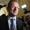 Man in suit and glasses at press conference surrounded by media cameras and microphones