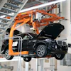 Black SUV suspended by orange mechanical lift in automotive manufacturing facility