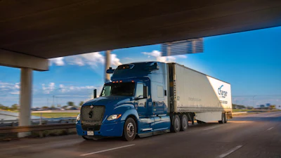 Blue Schneider semi-truck with white refrigerated trailer driving on highway under overpass