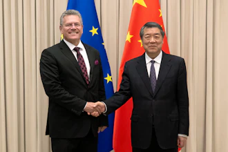 Two officials in formal business attire shake hands at a diplomatic meeting with EU and Chinese flags in the background.