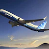 Boeing 737 aircraft in flight over mountainous landscape at sunset