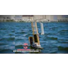 Autonomous solar-powered sailboat with white sails on blue water near waterfront buildings