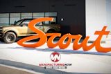 Scout Motors orange brand signage displayed outside showroom with tan SUV and Manufacturing Now logo