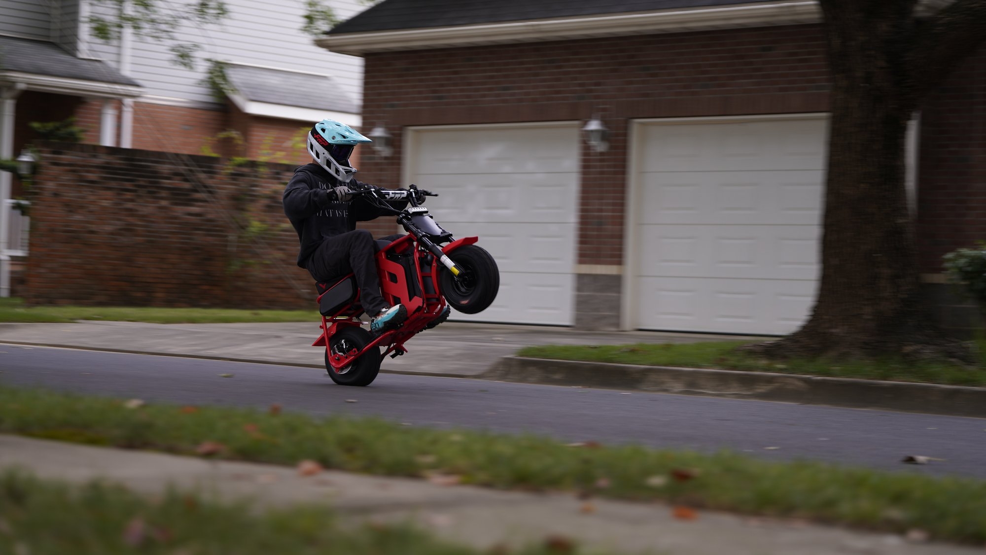 Stunt rider performing wheelie on red motorcycle in residential neighborhood street
