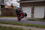 Stunt rider performing wheelie on red motorcycle in residential neighborhood street