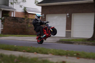 Stunt rider performing wheelie on red motorcycle in residential neighborhood street