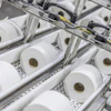 Industrial production line with multiple white tissue paper rolls on conveyor system with mechanical components and yellow wiring
