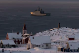 Arctic coastal settlement with red church, snow-covered buildings, and icebreaker ship in Greenlandic waters
