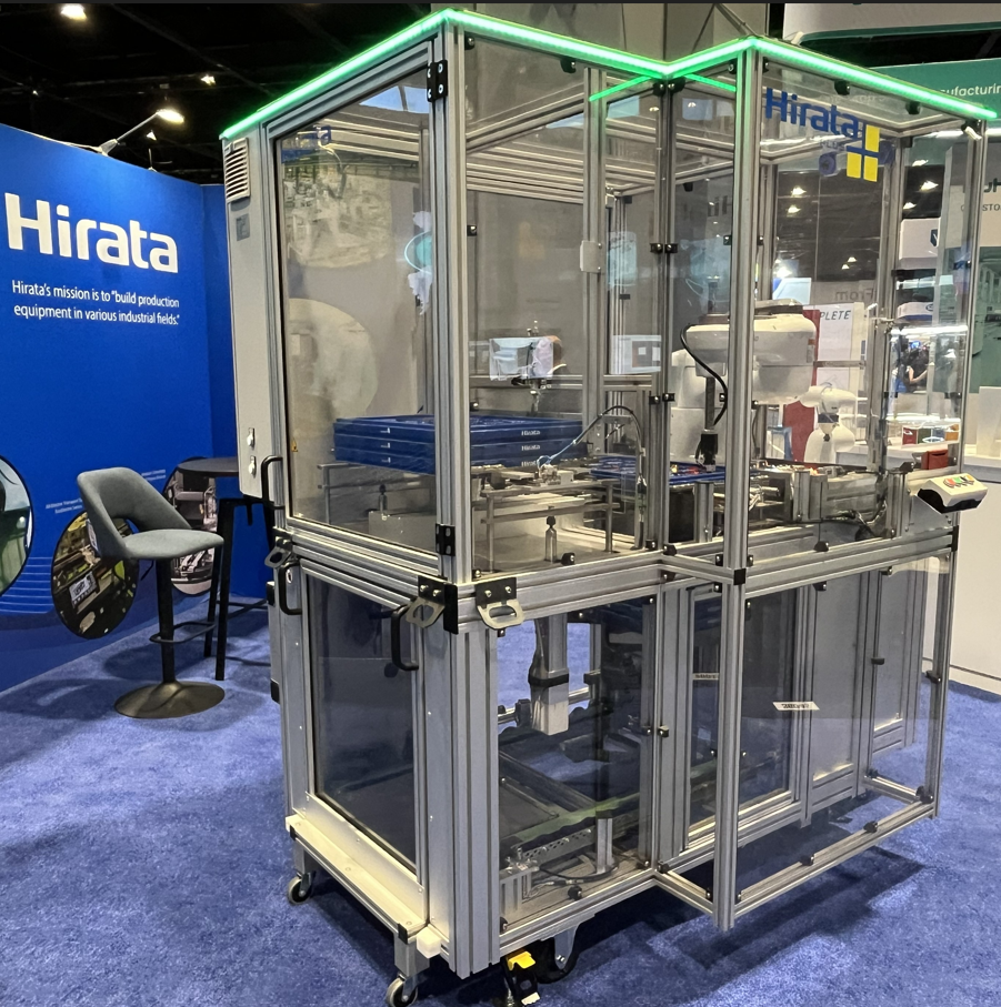Hirata industrial manufacturing equipment with transparent enclosure and green frame on blue trade show floor