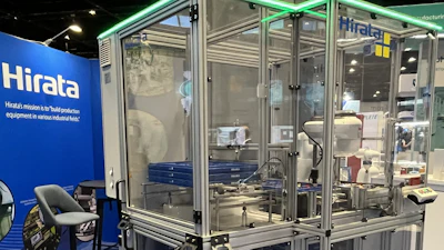 Hirata industrial manufacturing equipment with transparent enclosure and green frame on blue trade show floor