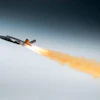 Fighter jet in flight with afterburners creating orange flame trail against blue sky