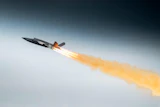 Fighter jet in flight with afterburners creating orange flame trail against blue sky