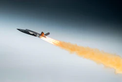 Fighter jet in flight with afterburners creating orange flame trail against blue sky