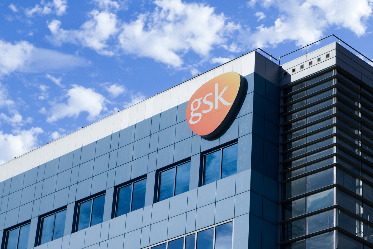 GSK corporate headquarters building with orange logo sign against blue sky and clouds