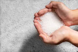 Hands holding white salt or sugar crystals against concrete background