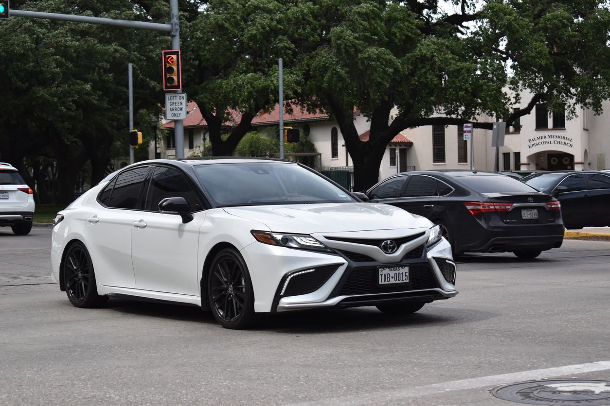 White Toyota Camry sedan parked on urban street with trees and buildings in background