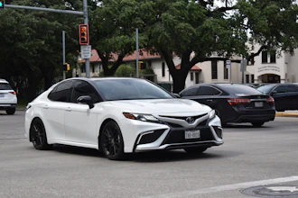White Toyota Camry sedan parked on urban street with trees and buildings in background