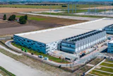 Aerial view of modern industrial warehouse complex with blue-accented buildings, loading docks, and surrounding agricultural landscape.
